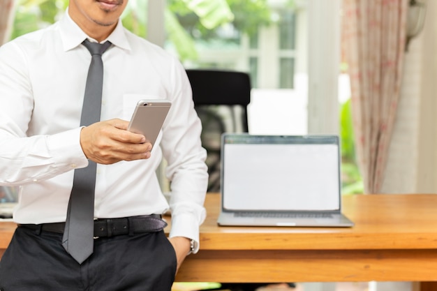 Homme d&#39;affaires en regardant un téléphone portable avec un ordinateur portable sur une table en bois au bureau