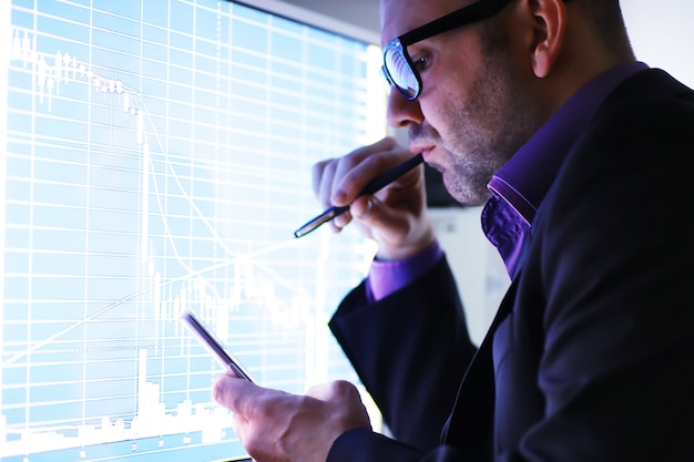 Un homme d'affaires regarde un graphique sur un moniteur. Un courtier en bourse évalue les tendances du marché boursier. Un homme à lunettes devant une courbe de la dynamique de l'économie.