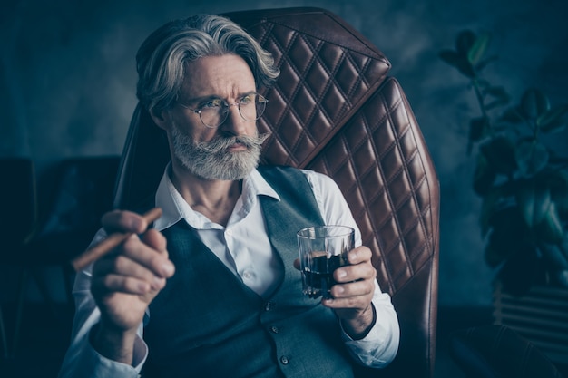 Homme d'affaires à la retraite fumer cigare boire du whisky dans le bureau gris loft