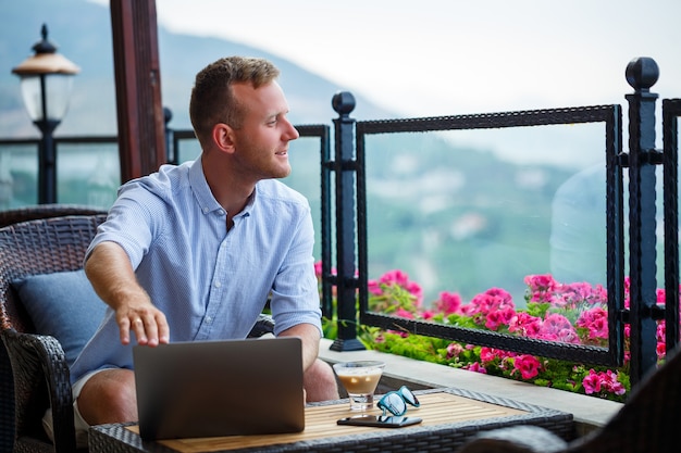 Homme d'affaires réussi travaillant en vacances derrière un ordinateur portable avec vue sur la montagne. Flux de travail du gestionnaire en ligne. Travaillez à l'extérieur avec une belle vue depuis le balcon