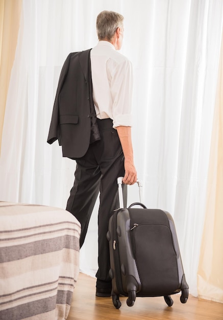 Homme d'affaires avec sa valise à la chambre d'hôtel en regardant la fenêtre Vue arrière