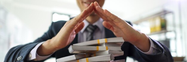 Un homme d'affaires satisfait fait une pyramide avec les mains au-dessus de piles d'argent assis à table au bureau