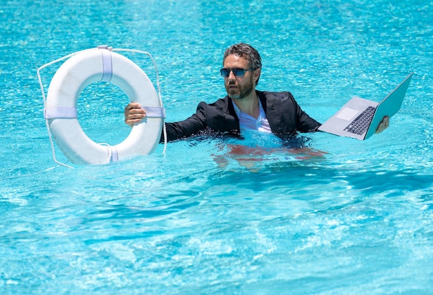 L'homme d'affaires de sauvetage en costume tient un ordinateur portable et une bouée de sauvetage dans la piscine de sauvetage ri