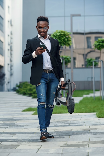 Homme d'affaires avec scooter électrique près du bâtiment d'entreprise moderne, parler au téléphone