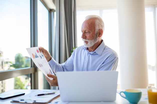 Homme d'affaires senior concentré présentant des tableaux et des graphiques lors d'un appel vidéo en ligne Homme d'affaires mature ayant une conférence téléphonique avec un client sur un ordinateur portable expliquant le fonctionnement de l'entreprise