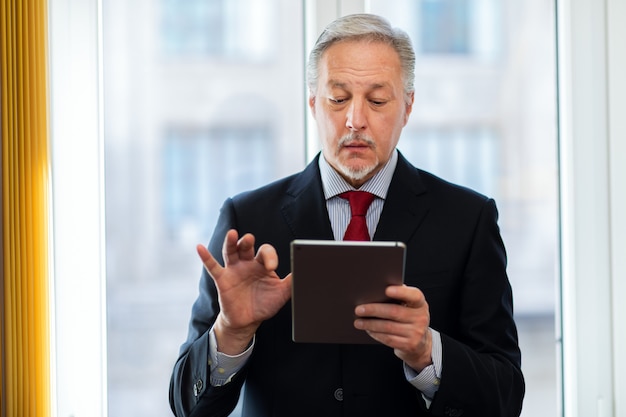 Homme d'affaires senior debout et tenant une tablette numérique à la main