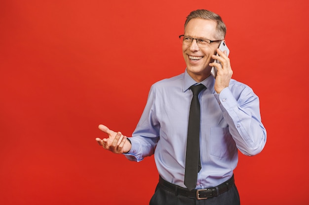 Photo homme d'affaires senior détendu en formel à l'aide de smartphone isolé sur mur rouge. portrait d'un homme d'affaires mature heureux à l'aide de téléphone portable. leader satisfait vérifiant le courrier avec copie espace.