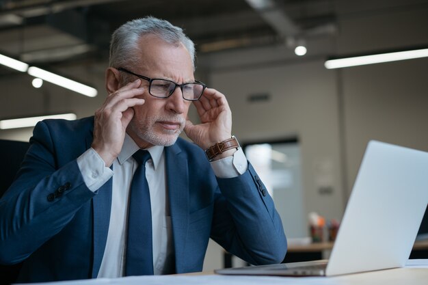 Homme d'affaires senior frustré à l'aide d'un ordinateur portable lisant des nouvelles travaillant au bureau