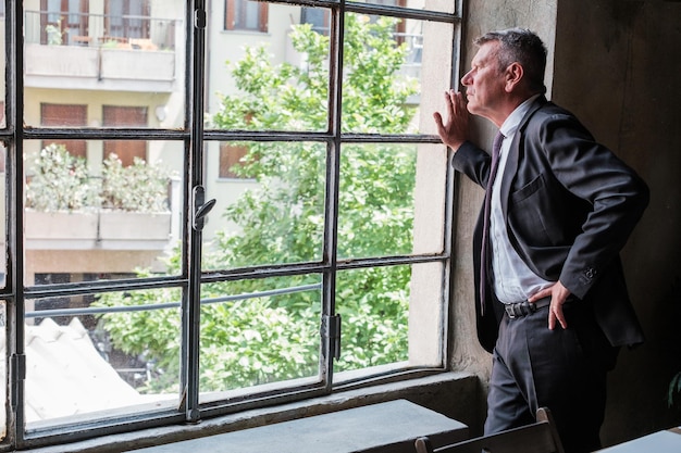 Homme d'affaires senior inquiet pour l'entreprise regardant par la fenêtre du bureau à la recherche de solutions