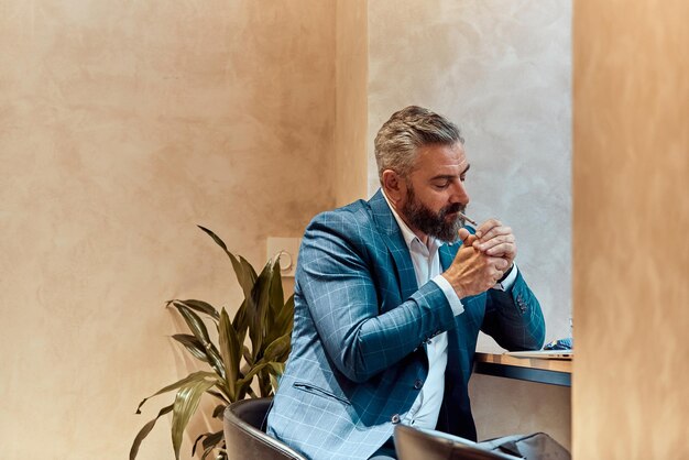 Homme d'affaires senior moderne fumant une cigarette tout en se reposant dans un café après une dure journée de travail.