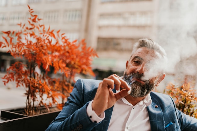 Un homme d'affaires senior moderne fume une cigarette tout en se reposant dans un café après une dure journée de travail