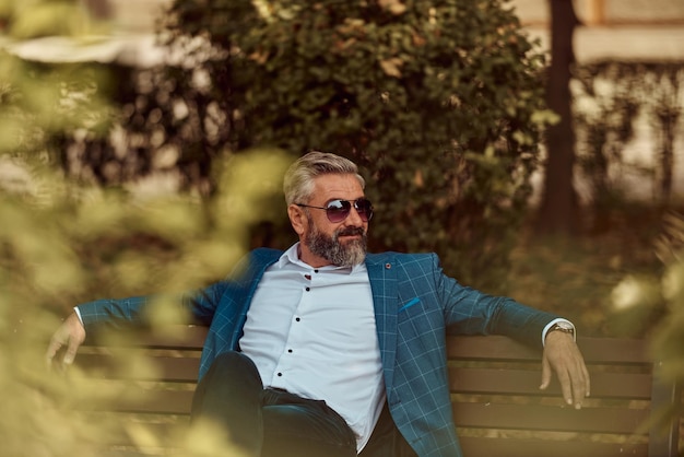 Homme d'affaires senior moderne reposant sur un banc dans la ville en pause de travail.