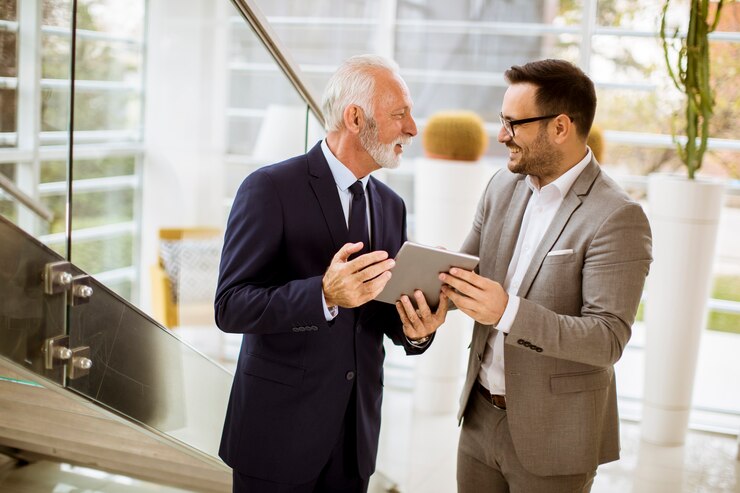 Photo homme d&#39;affaires senior montrant et montrant quelque chose à un partenaire junior sur une tablette numérique au bureau