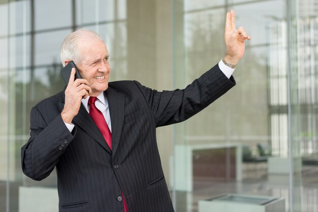 homme d&#39;affaires senior souriant en détournant les yeux, appelant sur smartphone et salutation