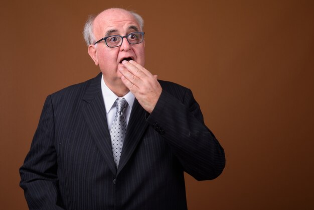 Homme d'affaires senior en surpoids portant des lunettes contre le mur marron