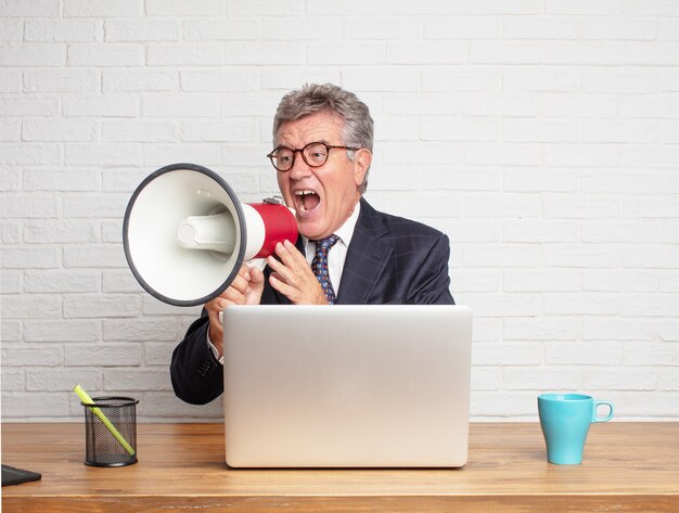 Homme d&#39;affaires senior travaillant avec son ordinateur portable et un mégaphone