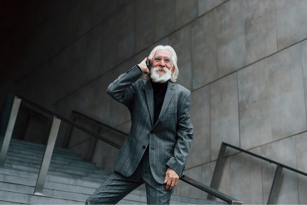 Un homme d'affaires senior en vêtements formels aux cheveux gris et à la barbe parle à l'extérieur par téléphone