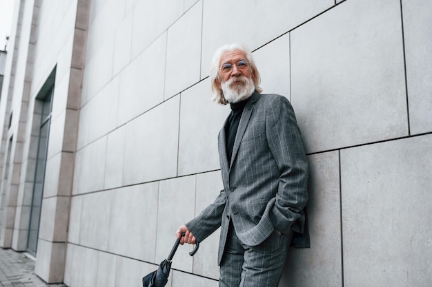 Un homme d'affaires senior en vêtements formels avec des cheveux gris et une barbe est à l'extérieur