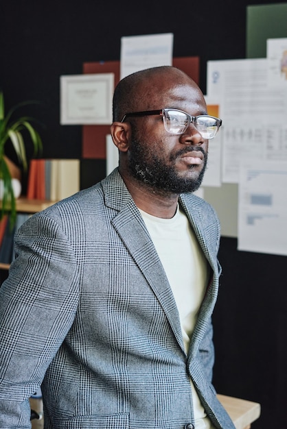 Photo homme d'affaires sérieux africain dans des lunettes semblant pensif tout en se tenant au bureau