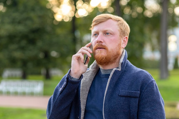 Photo homme d'affaires sérieux aux cheveux rouges. homme barbe, moustache parlant smartphone, mobile. guy pigiste barbu élégant à l'aide de téléphone