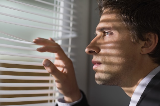 Homme d&#39;affaires sérieux furtivement à travers les stores dans le bureau