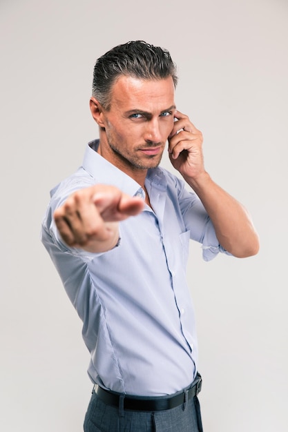 Homme d'affaires sérieux parlant au téléphone et pointant sur la caméra isolée