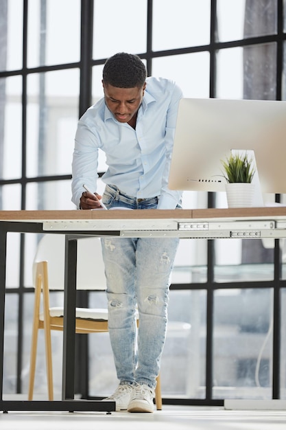 Homme d'affaires sérieux et réfléchi du millénaire, debout à la table, prenant des notes dans un cahier