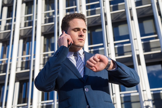 Homme d'affaires sérieux, vérifiant l'heure parler au téléphone.