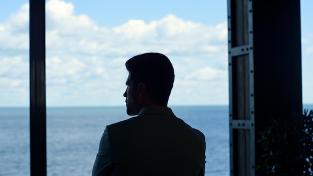 Homme d'affaires silhouette regardant la mer vue grande fenêtre