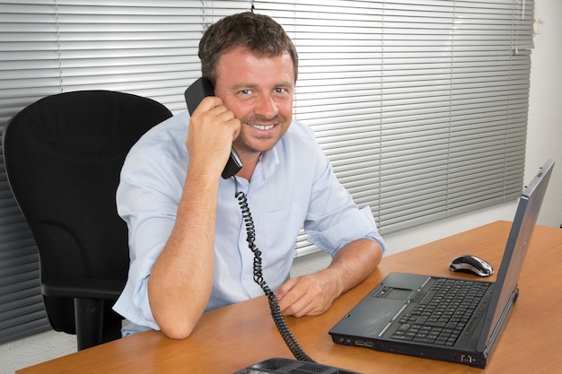 Homme d'affaires souriant à l'aide de téléphone et ordinateur portable au bureau