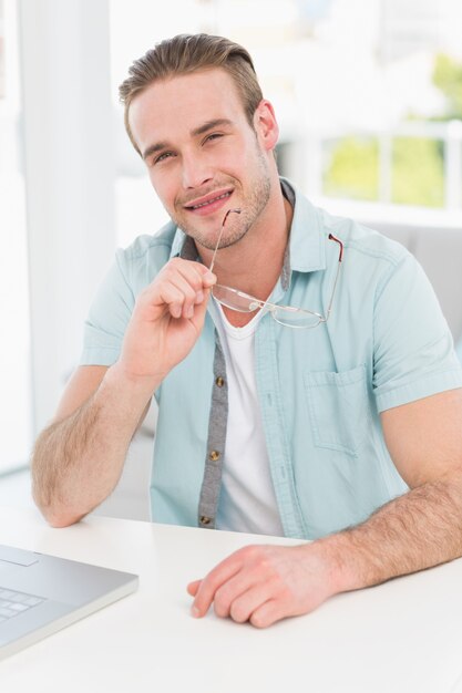 Homme d&#39;affaires souriant, assis à son bureau, tenant des lunettes