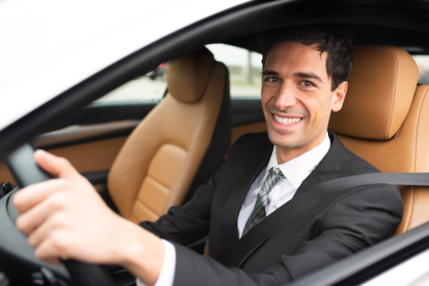 Homme d'affaires souriant au volant de sa nouvelle voiture blanche