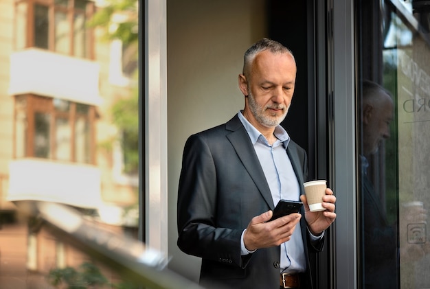 Homme d'affaires souriant en costume gris avec un smartphone.