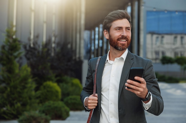 Homme d'affaires souriant en costume rentrant à la maison après une longue journée de travail et utilisant le téléphone