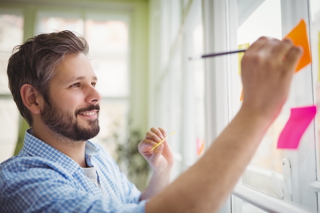 Homme d'affaires souriant écrit sur des notes adhésives au bureau