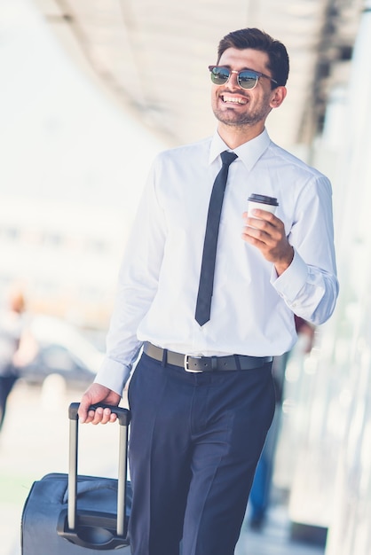 L'homme d'affaires souriant à lunettes de soleil marche avec une valise