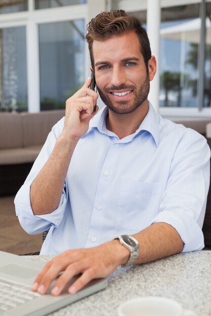 Homme d&#39;affaires souriant, parler au téléphone en utilisant son ordinateur portable