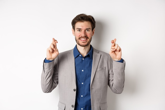 Homme d'affaires souriant plein d'espoir à la recherche optimiste, croiser les doigts bonne chance