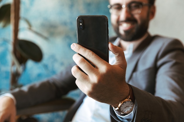 Homme d'affaires souriant portant costume tenant un téléphone portable alors qu'il était assis au café