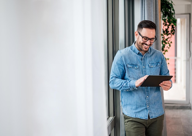 Homme d'affaires souriant portant des lunettes à l'aide d'une tablette informatique debout dans un espace d'affaires moderne