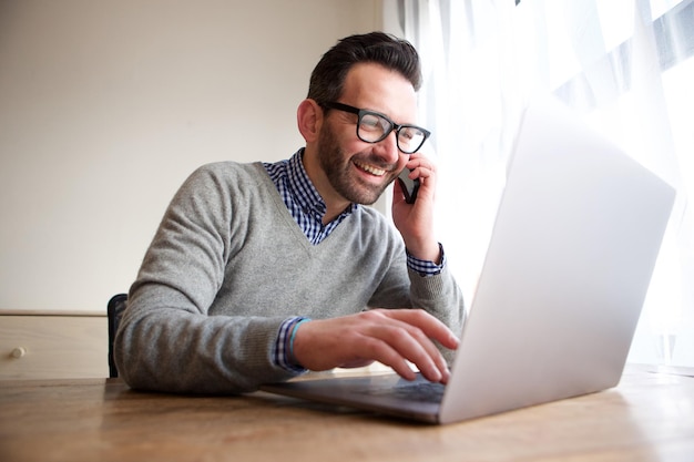 Un homme d'affaires souriant qui parle au téléphone portable et travaille à l'ordinateur.