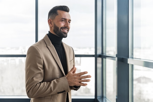 Un homme d'affaires souriant regarde par la fenêtre pendant qu'il est au bureau et se frotte les mains