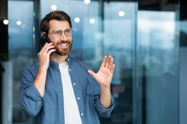 Homme d'affaires souriant réussi en chemise décontractée parlant au téléphone patron masculin dans les verres et la barbe près de