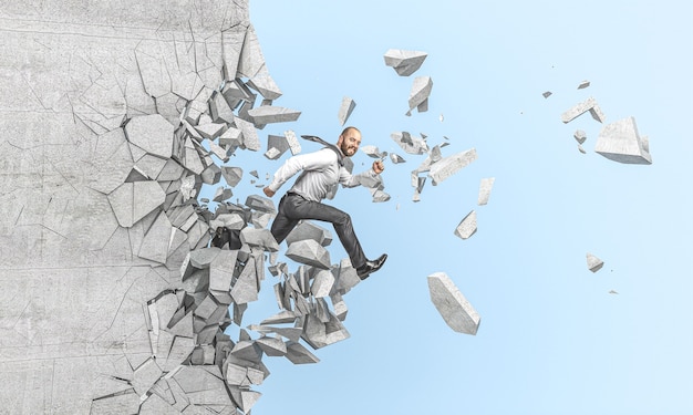 Photo un homme d'affaires souriant saute et traverse un mur de béton, concept de force et de détermination.