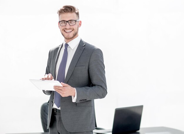 Homme d'affaires souriant avec tablette numérique debout près du bureau