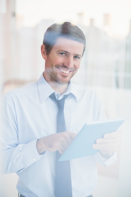 Homme d&#39;affaires souriant avec tablette regardant par la fenêtre