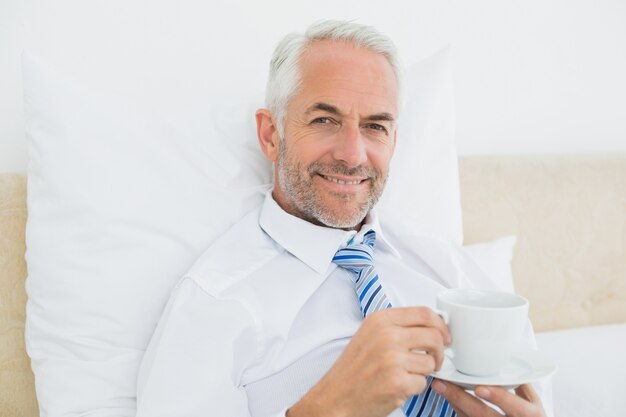 Homme d&#39;affaires souriant avec une tasse de thé au lit