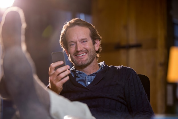 Homme d'affaires souriant tenant le téléphone portable au bureau