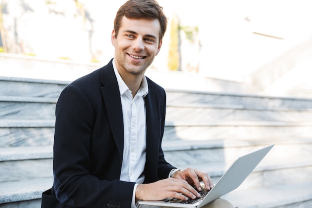 Homme d'affaires souriant travaillant sur un ordinateur portable à l'extérieur