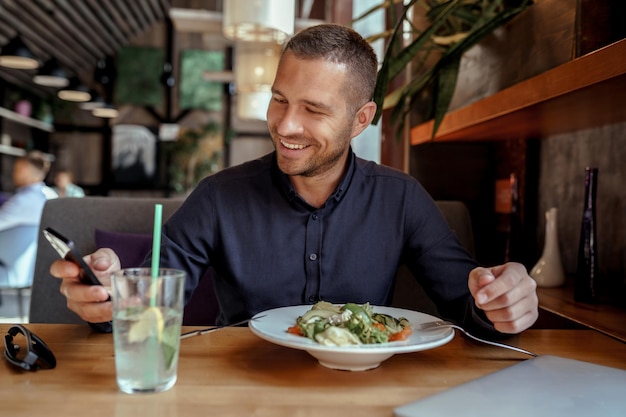 Un homme d'affaires souriant utilise son téléphone tout en déjeunant au restaurant